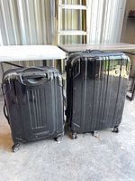 Front view of both black hardshell suitcases side by side showing overall design and wear