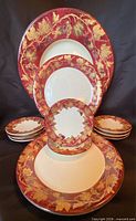Front view showing all eleven plates arranged by size, displaying red and gold grapevine motif