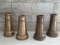 Front view of four brass fire hose nozzles standing upright showing patina and threaded openings