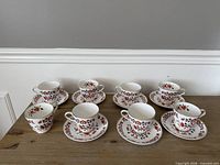 Eight tea cups and saucers displayed on table; shows overall quantity and pattern