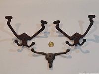 Two ornate triple-arm hooks, longhorn steer hook, coin for scale