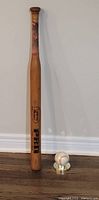 Full view of signed wooden bat standing upright next to signed baseball on display stand