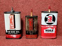 Front view of three 3-In-One oil tins showing branding and condition