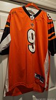 Front view of orange Bengals #9 jersey on hanger showing signatures