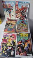 Six comics laid out including Avenging Spider-Man, DC Legends, Justice League