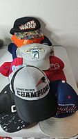 Stack of assorted caps showing Star Wars, Chicago Bears, camouflage, gray World Champions, red FG and Patriots caps
