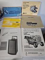 Six manuals laid out showing covers for Cadillac, Zenith, Chevy Van, Sears Kenmore sewing machine, Califone PA-750 and Snapper LT2502/LT1602