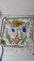Front view of white Masonic apron showing main design and fringe