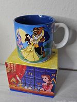 Front view of mug on top of box showing Belle and Beast dancing