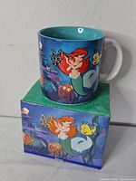 Front view of mug on box showing Ariel and Flounder artwork