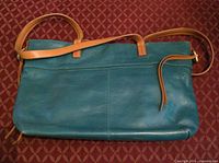 Front view of teal leather Hobo crossbody with tan strap on patterned surface