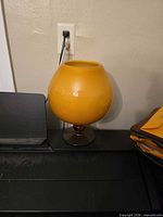 Front view of spherical orange cased glass vase on pedestal base