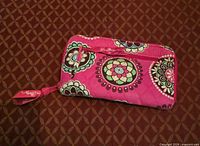 Front view of pink floral quilted wallet showing exterior zip pocket and wrist pull tab