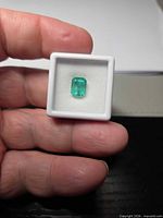 Emerald in display box held between fingers showing overall size and color