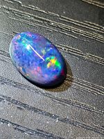 Front view of oval black opal showing play of colour