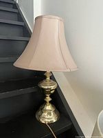 Full view of brass table lamp with beige shade on staircase