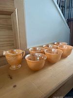Six peach lustre cups and matching creamer on shelf