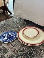 Overview of stacked cream/red plates, blue willow plate, clear glass bowl inside pie plate