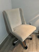 Front angled view of cream upholstered office chair showing nailhead trim and chrome base