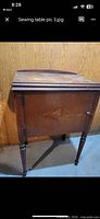 Side view of closed wooden sewing machine cabinet on legs showing arrow inlay