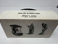 Box top showing Snow Village First Round of the Year text and silhouette images