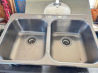 Full view of double bowl stainless steel sink showing basins, drain assemblies and 3-hole faucet deck