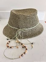 Side view of crocheted olive paper straw hat with beaded tassel cord