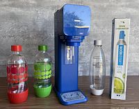 Full view of blue SodaStream machine, three bottles and boxed carbonator