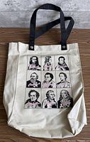 Full front view of off-white canvas tote bag showing handles and printed design