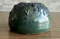 side view showing green glaze and black drip texture of low vase