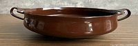 Profile view of brown enameled paella pan showing height and handles