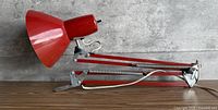 Full side view of red articulating desk lamp showing arms, springs, shade, clamp base