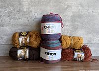 Group shot showing all five skeins: four Heartland in various colors flanking one Caron Cakes