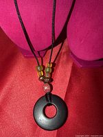 Full view of necklace on display bust showing black silk cord, bead arrangement, and wood pendant