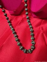 Full view of hunter-green silk bead necklace on display stand