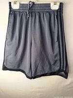 Front view of gray and black Adidas youth shorts hanging on clips