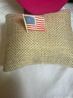 Front view of American flag lapel pin on burlap cushion
