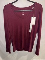 Front view of burgundy long sleeve scoop neck top on hanger showing tags