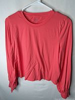 Front view of coral long-sleeve crew-neck shirt hanging