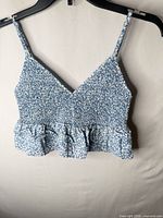 Front view of blue and white floral smocked crop camisole with ruffle hem on hanger