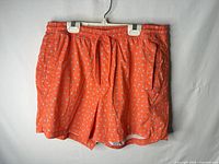 Full front view of orange bird-print swim trunks on hanger