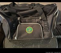 Full view of black duffel bag front showing embroidered Archbishop Wood High School crest and white-piped front zip pocket