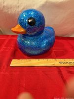 Full view of glitter blue duck coin bank beside ruler for scale