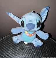 Front view of blue Stitch plush seated on wicker table