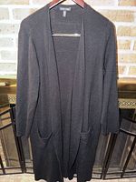 Front view of long black open cardigan on hanger showing full length and pockets