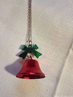 Front view of red bell pendant with green bow on silver-tone chain