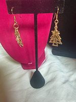 Front view of both gold-tone Christmas tree dangle earrings on display stand