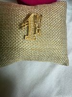 Front view of gold-tone "#1 MOM" lapel pin on cushion