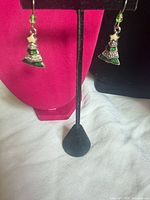 Both earrings hanging from stand showing Christmas tree design, enamel colours, bead accents and hooks