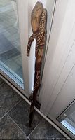 Full view of carved wooden walking stick leaning against glass door